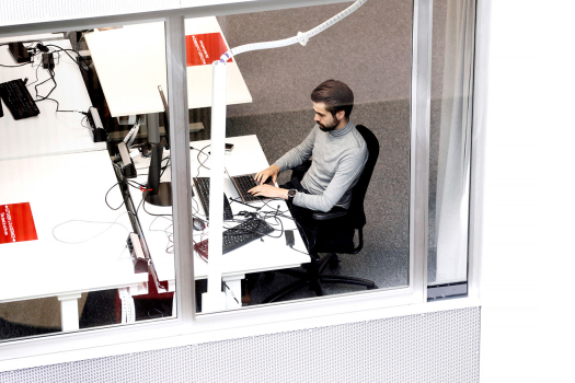Ylhäältä kuvattu parrakas mies istuu työpöydän ääressä ja tekee töitä tietokoneella