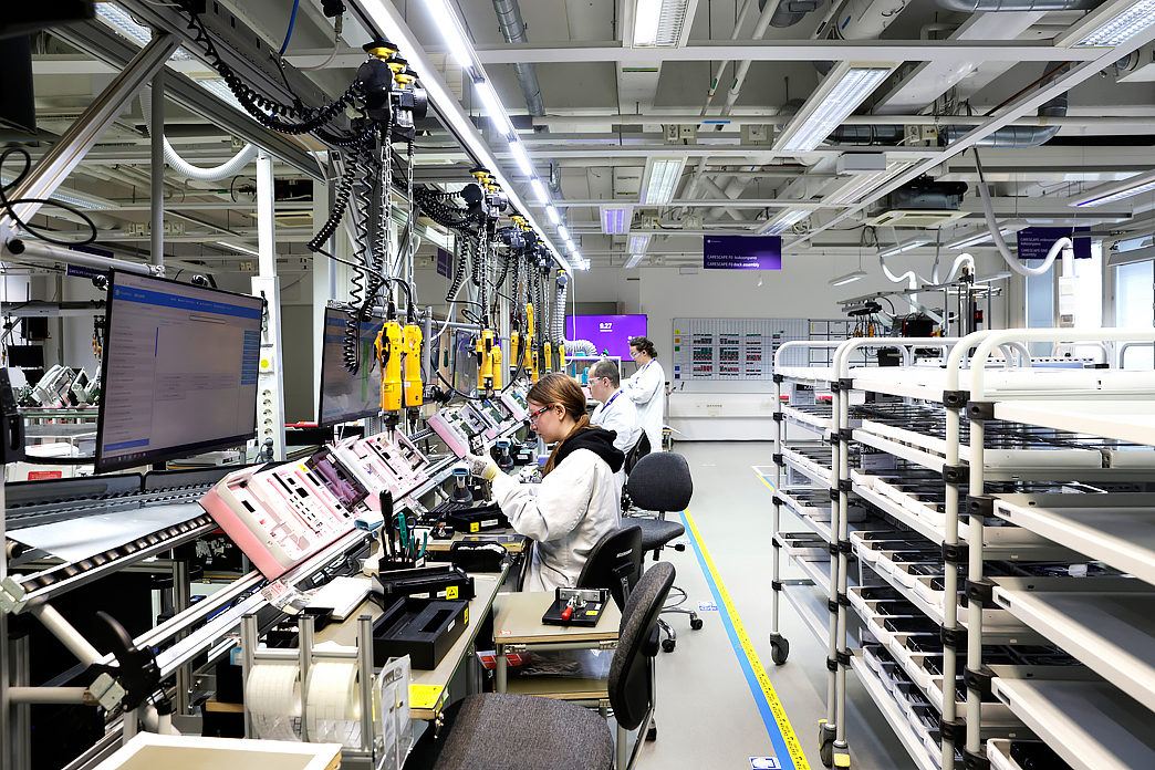 Henkilöt työskentelevät tehtaassa linjastolla vierekkäin, kuvituskuva.