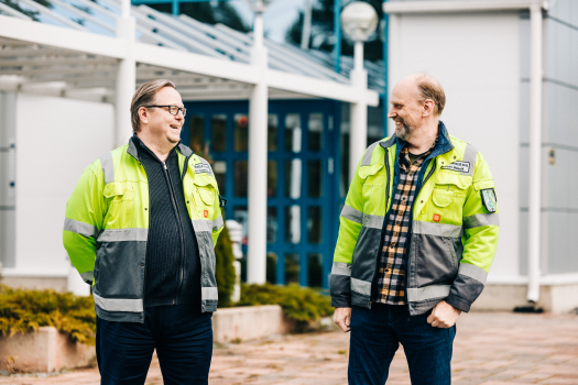 Mäkelä Alun toimitusjohtaja toimitusjohtaja Marko Orpana ja hallituksen puheenjohtaja Petri Mäkelä seisovat tehdasrakennuksen edessä ja nauravat.