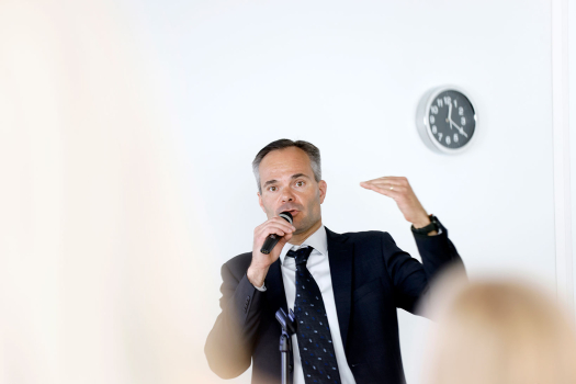 Ympäristö- ja ilmastoministeri Kai Mykkänen puhuu mikrofoniin, kuvan etualalla näkyy yleisön päitä.