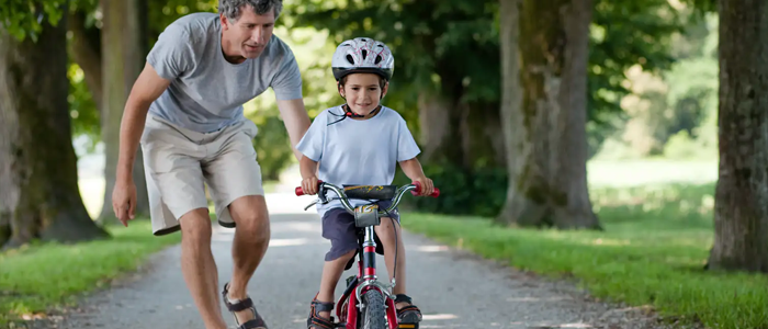 Aikuinen auttaa lasta kehittymään pyöräilemisessä ilman apupyöriä.