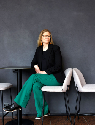 Capgeminin henkilöstöjohtaja Leena Kirjavainen istuu valkealla tuolilla siniharmaata seinää vasten.