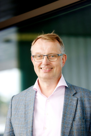 Toimitusjohtaja Jukka Leskelä hymyilee harmaa puku ja vaalea paita päällä.