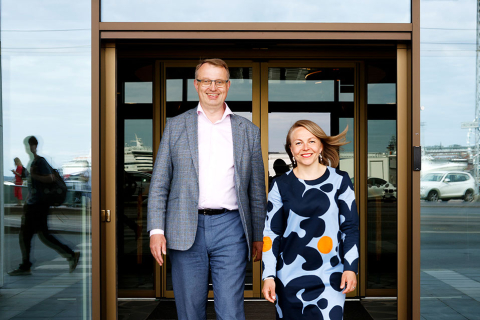 Jukka Leskelä ja Annukka Saari seisovat ulko-ovella ja hymyilevät.  