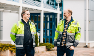Mäkelä Alun toimitusjohtaja toimitusjohtaja Marko Orpana ja hallituksen puheenjohtaja Petri Mäkelä seisovat tehdasrakennuksen edessä ja nauravat.