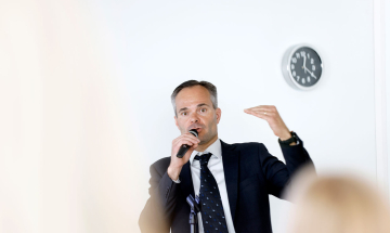 Ympäristö- ja ilmastoministeri Kai Mykkänen puhuu mikrofoniin, kuvan etualalla näkyy yleisön päitä.
