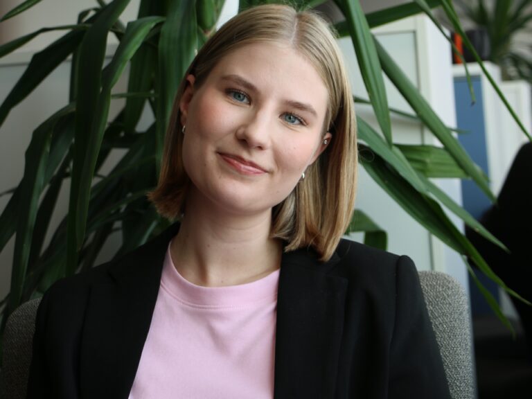 Nainen katsoo kameraan ja hymyilee.