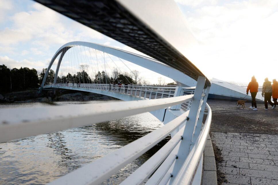 Valkea kaarisilta veden yllä, taustalla kävelijöitä ja koiranulkoiluttajia.