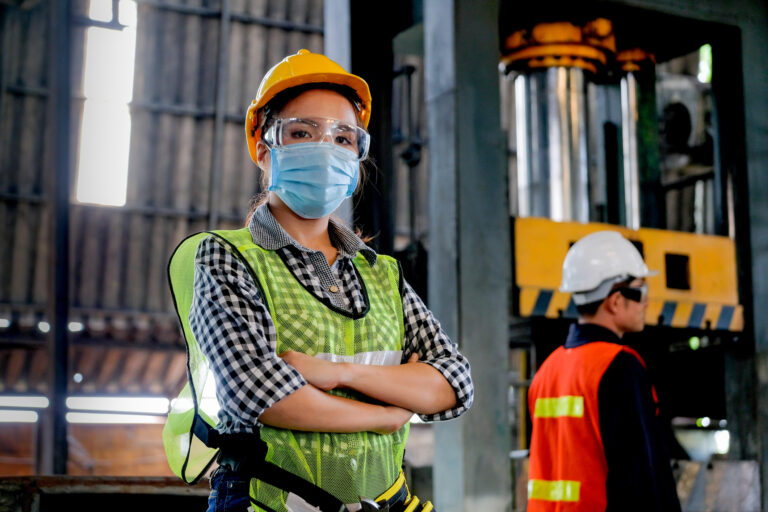 Factory woman worker or technician with hygienic mask stand with confident action with her co-worker as background.
