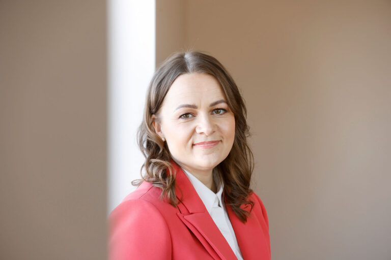 Nainen punaisessa jakussa katsoo kameraan.