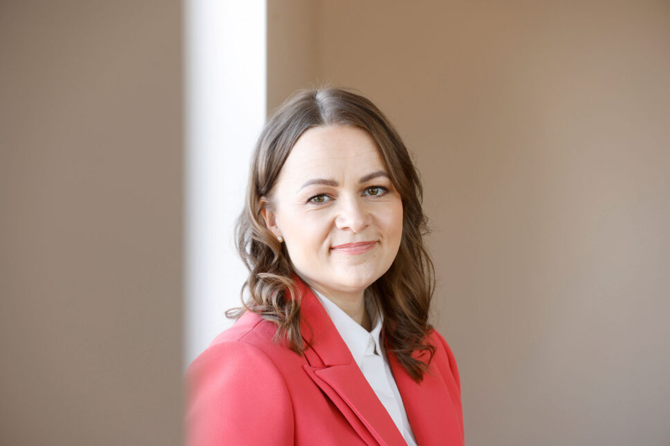 Nainen punaisessa jakussa katsoo kameraan.