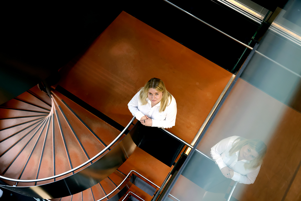 Vaalea nainen valkoisessa paidassa kuvattu puurakenteisissa rappusissa yläpuolelta.