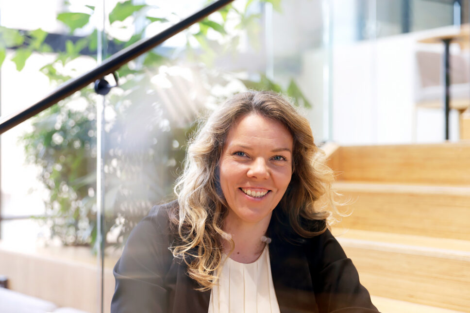 Tummahiuksinen nainen istuu vaalealla puuportaikolla ja hymyilee.