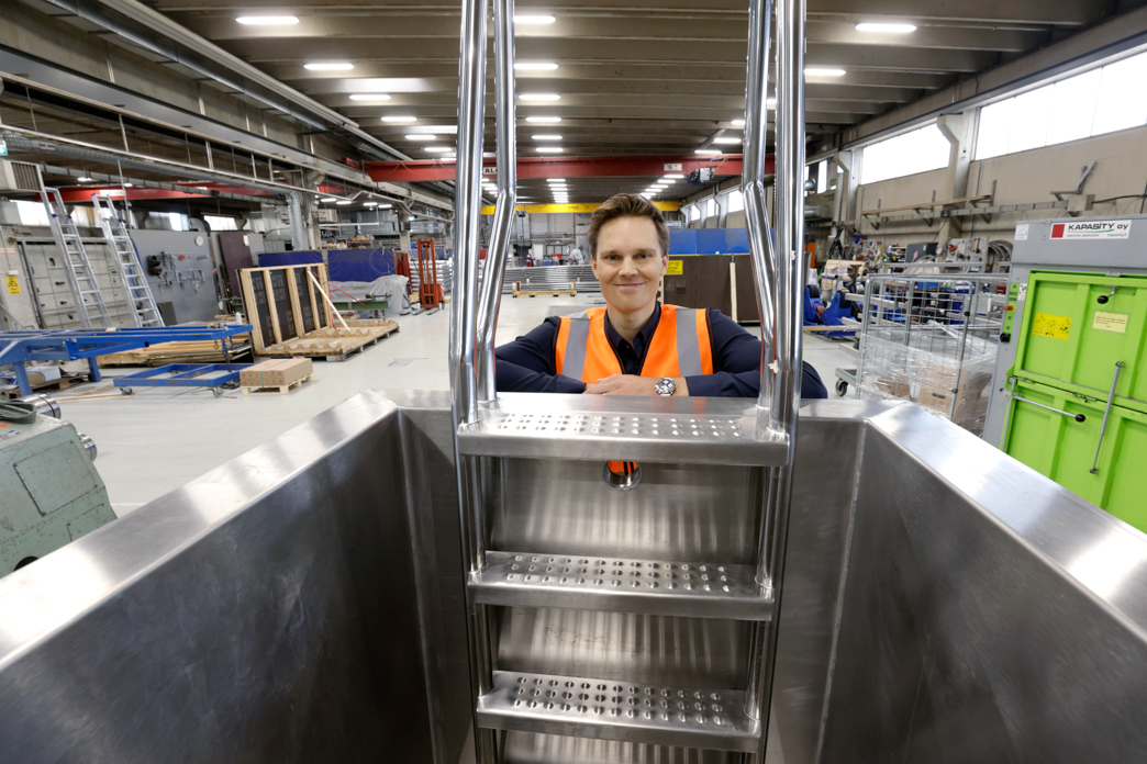 Suojaliiveihin pukeutunut mies hymyilee teräksisen kylmäaltaan äärellä.