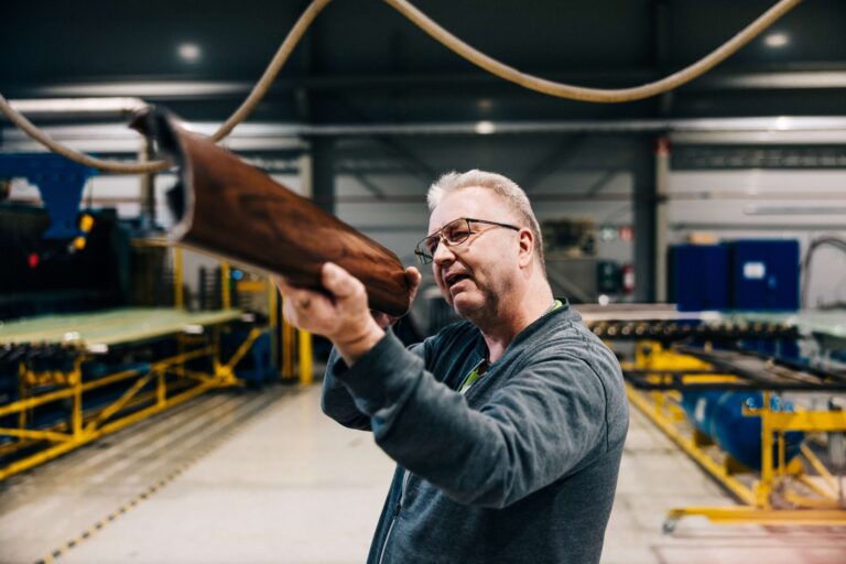 Mies tähtää tehdassalissa kuvan ulkopuoliselle kiiltävällä alumiiniprofiililla.