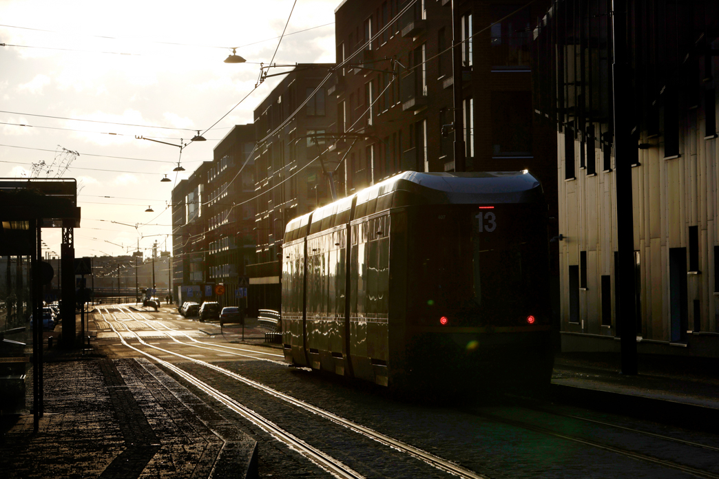 Raitiovaunu ajaa kohti auringonnousua, taustalla moderneja kerrostaloja