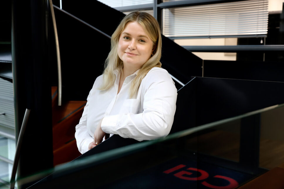 Blonde woman in white shirt leaning on black rail.