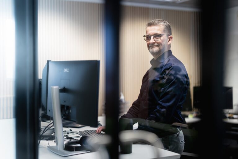 Mies seisoo toimistossa tietokoneen ääressä.