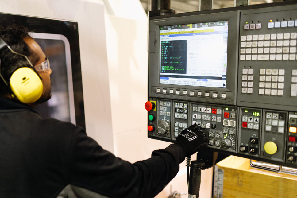 Kuulosuojaimilla varustettu, mustiin pukeutunut työntekijä painaa näyttötaulun nappuloita.