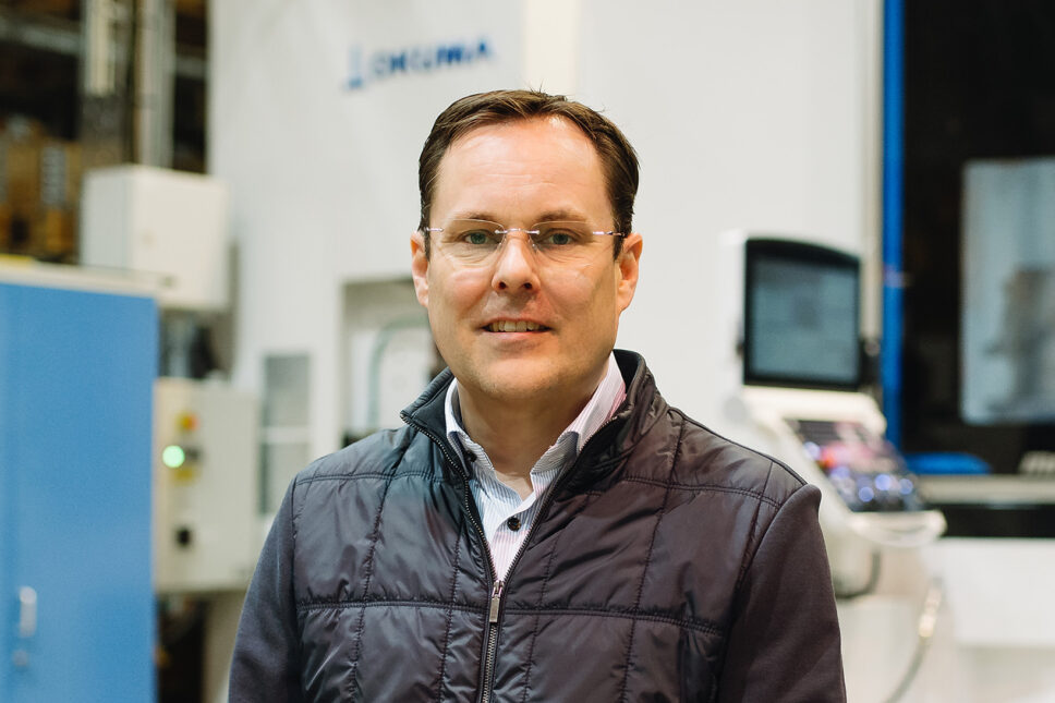 Silmälasipäinen mies katsoo lähikuvassa kameraan ja hymyilee.