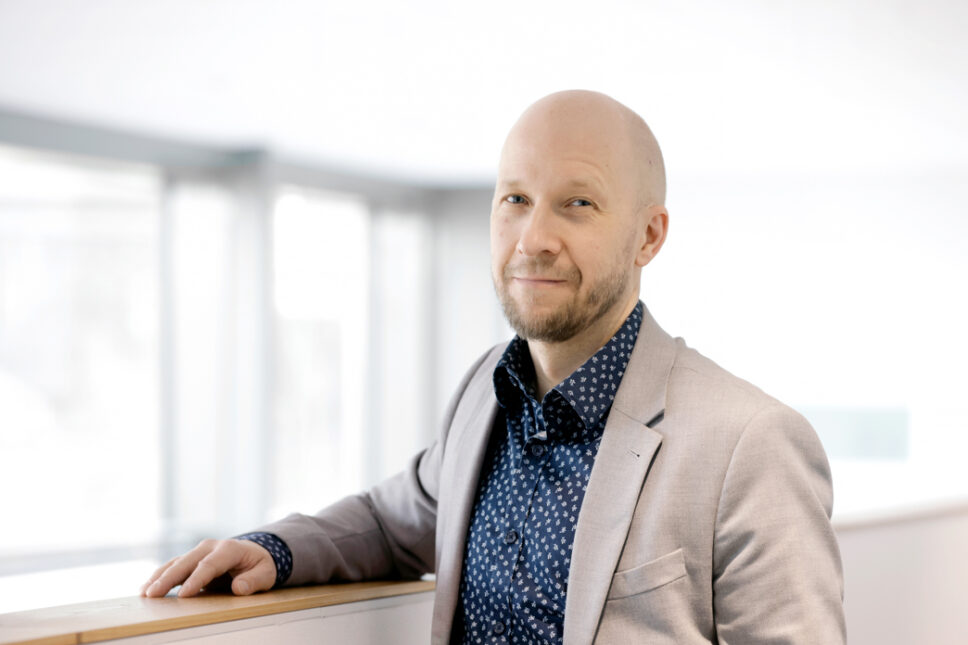 Vaaleapukuinen mies nojaa kaiteeseen ja katsoo kameraan.